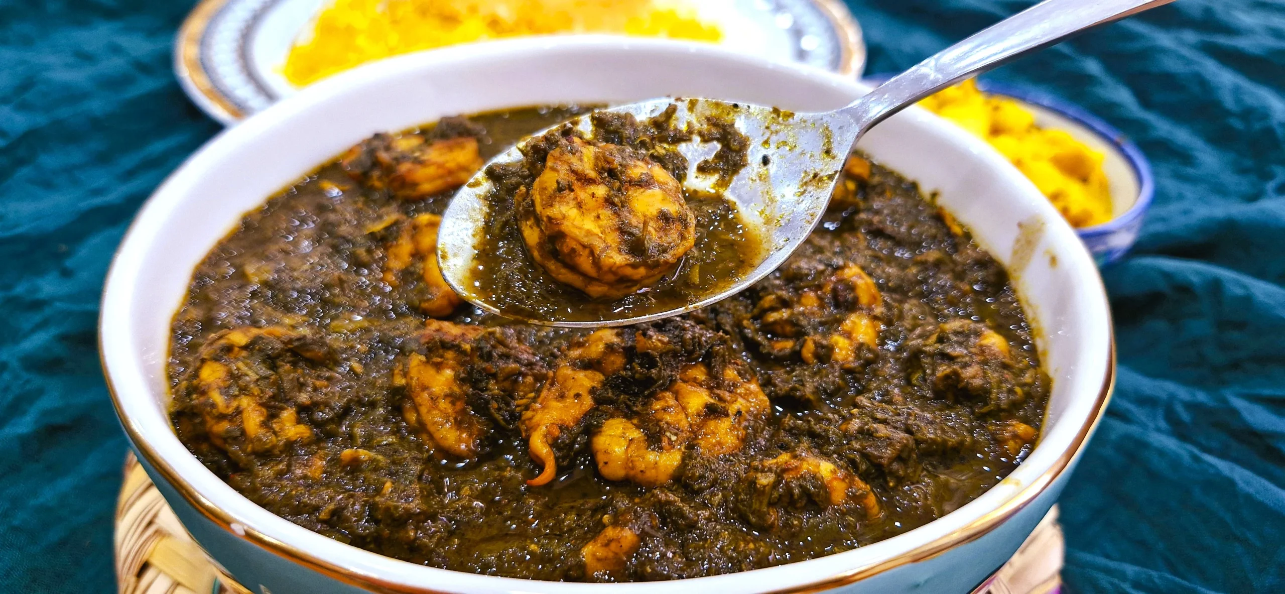 Ghalieh Meygoo Close-Up Close-up of Ghalieh Meygoo with a shrimp in a spoon, showing the rich herb and tamarind sauce