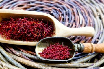 Dried Persian saffron threads in wooden and metal scoops on a woven mat