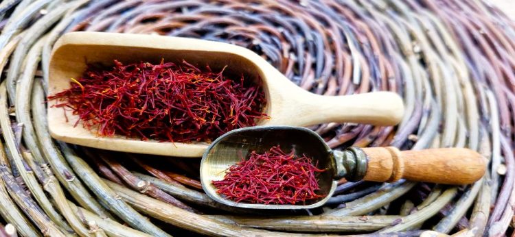 Dried Persian saffron threads in wooden and metal scoops on a woven mat